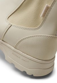 Botas beige con suela de goma texturizada, parte superior lisa, paneles de tela elástica y el logo grabado "NATURAL SOFT™".