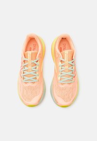 Baskets de course légères en mesh pêche avec des lacets et des accents turquoise. Elles présentent une semelle rembourrée avec des détails réfléchissants et une surface texturée.