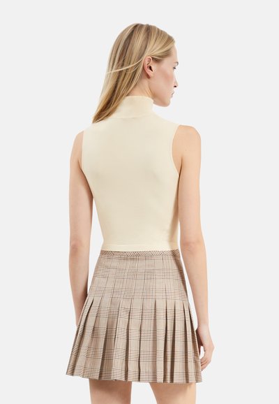 Top crema a collo alto abbinato a una gonna plissee a quadri nei toni beige, marrone e blu navy. La gonna presenta numerosi plissè e una vita aderente.