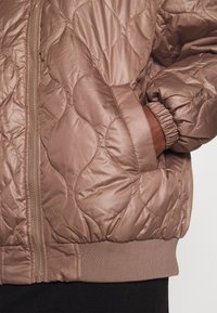 Quilted bomberjakke i dæmpet rosa med en skinnende satinfinish, elastiske manchetter og frontlynlås. Blød tekstur med en hyggelig pasform.