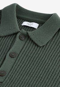 Grøn strikket polo t-shirt med en tekstureret stof, med krave, tre mørke knapper og et mærke med logo ved halsen.