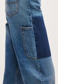 Τζιν παντελόνια με σχέδιο πατς από ανοιχτό και σκούρο μπλε κομμάτια, με μικρή πίσω τσέπη και ραφές ως διακοσμητικά στοιχεία.