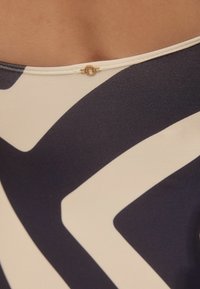 Marineblauw en crème ééndelige swimsuit met een geometrisch patroon. Geweven stof met een gouden detail bij de sluiting op de rug.