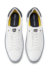 Sneaker in pelle bianca con design semplice, punta tonda, dettagli testurizzati in blu navy e lacci bianchi. Sottopiedi gialli e blu navy con logo del marchio.