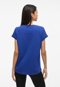 Královsky modré tričko s krátkým rukávem, kulatým výstřihem a volným střihem. Hladká textura a mírně zakulacený lem vzadu.