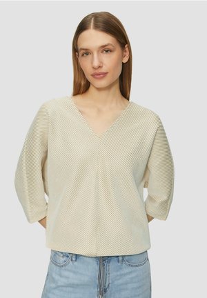 Haut beige clair à col en V avec des rayures horizontales, manches trois-quarts et coupe décontractée, associé à un jean en denim bleu clair.