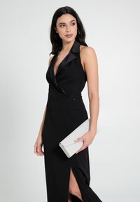 Schwarzes Neckholder-Kleid mit tiefem Ausschnitt und seitlichem Schlitz. Begleitet von einer silbernen Glitzer-Clutch mit elegantem Design.