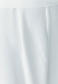 Witte stof met een gladde textuur en subtiele glans. Voorzien van plooien aan de voorkant, die een zachte drapering creëren. Lichtgewicht en vloeiend ontwerp.