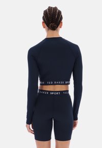 Tengerészkék sportkészlet hosszú ujjú, rövid felsővel és magas derekú nadrágban, kontrasztos, márkázott elasztikus derékszalaggal és sima textúrával.