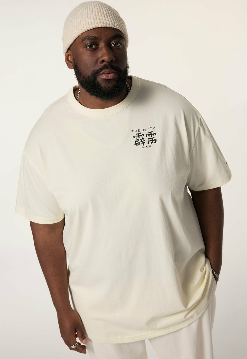 Světle béžové oversized tričko s krátkými rukávy a kulatým výstřihem, na levé části hrudi má černý grafický potisk.