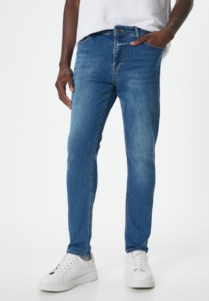 Strakke blauwe spijkerbroek met een licht vervaagde afwerking, vijf zakken en een knoopsluiting. Gepaard met witte sneakers.