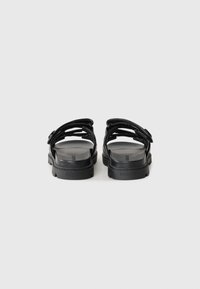 Black sandals with multiple straps, a textured sole, and a flat design. Features a logo embossed on the footbed and adjustable buckles.