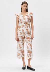 Biała lniana stylizacja z pomarańczowymi kwiatowymi wzorami. Bluzka posiada dekolt w serek oraz falbany na rękawach; spodnie są 7/8 o prostym kroju. Całość dopełniają czarne baleriny.