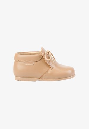 Bota de cuero beige hasta el tobillo con borde ondulado y cierre de cordones. Punta redondeada y textura suave, diseñada para comodidad y durabilidad.