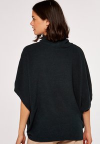 Pull à col haut en vert foncé, oversize, avec des manches chauve-souris. Texture douce, poignets et ourlet côtelés. Design uni, avec un minimum de détails.