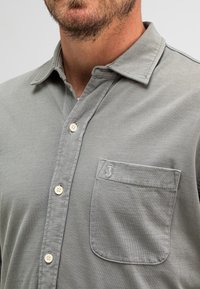 Grijze katoenen button-up shirt met een zak. Heeft een klassieke kraag en beige knopen met een subtiel logo op de zak. Zachte textuur.