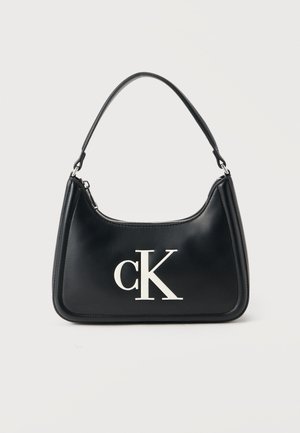 Fekete bőr táska lekerekített formával, elülső részén fehér "cK" logóval és rövid fekete pánttal. Simább tapintású, cipzáras záródással.