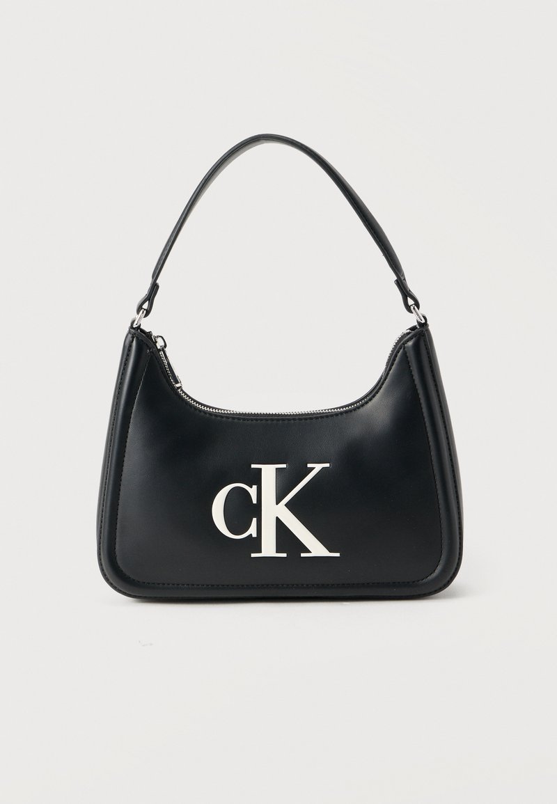 Μαύρη δερμάτινη τσάντα χειρός με στρογγυλεμένο σχήμα, που διαθέτει λευκό λογότυπο "cK" στο μπροστινό μέρος και κοντό μαύρο λουράκι. Λείο υλικό και κλείσιμο με φερμουάρ.
