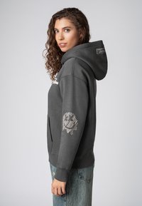 Grijze hoodie met voorzak, voorzien van een patroon op de linker mouw. Gemaakt van gestructureerde stof met geribbelde manchetten.