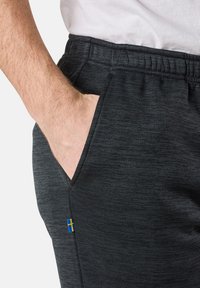 Dunkelgraue Sporthosen aus einem strukturierten Stoff, mit Seitentaschen und einem kleinen schwedischen Flaggen-Detail an der unteren linken Seite.