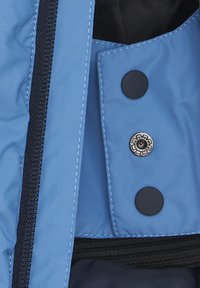 Blaues Oberbekleidungsstück mit glatter Textur, ausgestattet mit einem schwarzen Reißverschluss und zwei runden schwarzen Knöpfen, von denen einer metallisch und mit einem dekorativen Design versehen ist.
