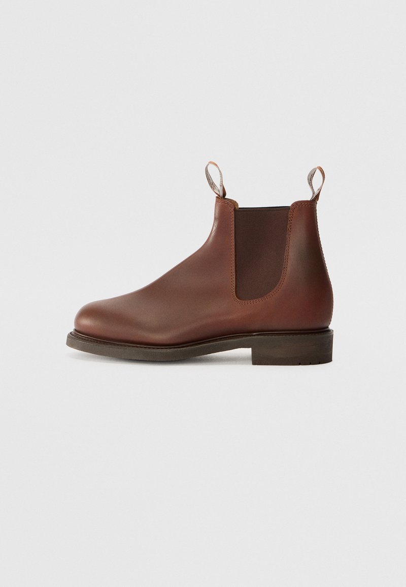 Botte Chelsea en cuir marron avec panneaux élastiques sur les côtés, une languette à l'arrière et un petit talon empilé. Texture lisse avec bout arrondi et un design minimaliste.