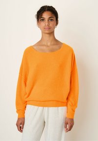 Orange oversized sweater med bred halsudskæring og lange ærmer, lavet af et textured strikket stof, parret med lysegrå bukser.