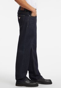 Jeans in denim blu scuro con vestibilità dritta, dettagli di cucitura visibili e tasche laterali. Si abbinano bene con scarpe nere.