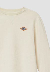 Crème-kleurig sweatshirt met ribbelstructuur, voorzien van een ruitvormige patch in blauwe en oranje stiksel op de borst.