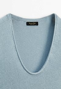 Vaaleansininen neulepaita, jossa on V-pääntie. Tekstuuri on sileä, hieno ja tasainen ommelkuvio. Tarrassa lukee "Massimo Dutti, valmistettu Turkissa."