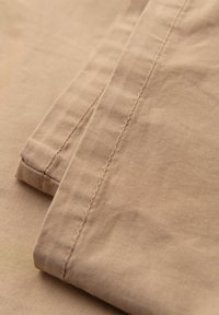 Nærbillede af beige stof med synlige syninger på foldede beklædningskanter, der fremhæver tekstur og sømdetaljer.