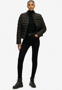 Czarna kurtka puchowa z wysokim kołnierzem, czarny dopasowany golf i czarne slim fit dżinsy, w zestawie z czarnymi sznurowanymi butami wojskowymi.