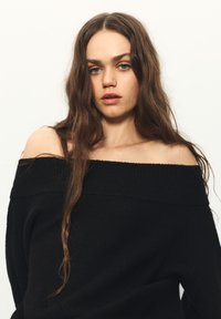 Schwarzer schulterfreier Pullover aus weichem Strickstoff mit geripptem Rundhalsausschnitt. Langer, weiter Schnitt mit leichter Struktur, lässig getragen.