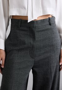 Pantaloni grigi su misura in tessuto testurizzato, con vita piatta, due tasche laterali e una vita aderente, abbinati a una camicia bianca.