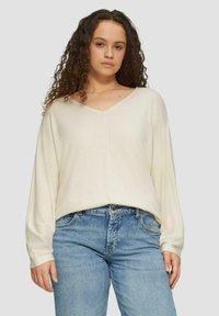 Cremefarbener V-Ausschnitt-Pullover mit langen Ärmeln, weichem Textil, leicht lockerer Passform, kombiniert mit hellblauen Denim-Jeans. Schlichtes und lässiges Design.