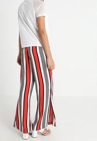 Pantalones palazzo a rayas con rayas verticales en negro, rojo y blanco, fabricados con tela ligera; combinados con una blusa de manga corta.