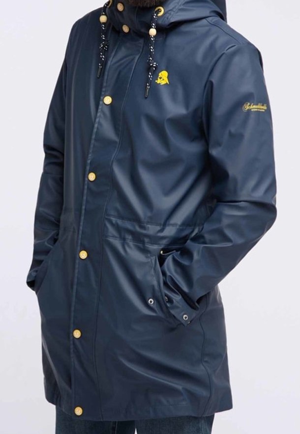 Marinblå vattentät jacka med huva, guldknappar, justerbara dragsnören och sidofickor. Slät textur med en logotyp på bröstet.