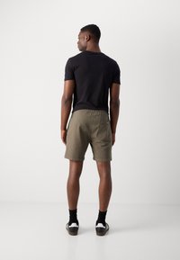 Mørk kortærmet t-shirt parret med olivengrønne shorts med elastisk talje og baglomme. Modellen har sorte sokker og sneakers på.