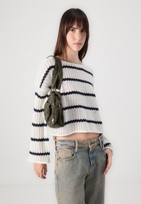 Suéter de punto blanco, corto, con rayas marinas, combinado con jeans de un azul claro desvanecido y un pequeño bolso color oliva en el hombro.