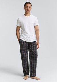 T-shirt blanc assorti à un pantalon de pyjama à carreaux avec des couleurs bleu foncé, vert, rouge et beige. Le tissu semble doux et confortable.