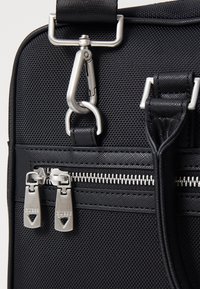 Borsa nera con texture, dotata di una chiusura in metallo argento, doppie zip con logo e un design elegante per un utilizzo pratico.