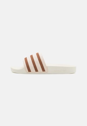 Sandale slide beige avec trois bandes marron sur la large bride en tissu et une semelle plate.