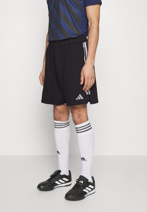 Shorts sportivi neri con righe bianche, abbinati a calze bianche fino al ginocchio e scarpe sportive nere con dettagli bianchi.