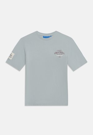 T-shirt gris clair à manches courtes avec le texte "GRACIOUS Redefined Rebel RBL" sur la poitrine et une petite étiquette sur la manche gauche.