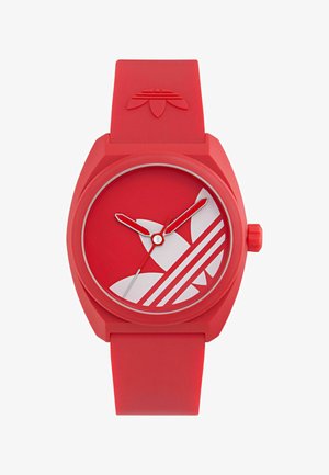 Piros szilikon karóra kerek számlappal, fehér Adidas logóval, fehér óragyűrűkkel és piros óra- és percmutatókkal. Forgatható korona az oldalán.