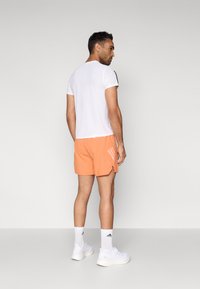 Ανδρικό αθλητικό σύνολο με λευκό κοντομάνικο πουκάμισο, πορτοκαλί σορτς και λευκά αθλητικά παπούτσια με τρεις ρίγες. Απλός σχεδιασμός και ελαφρύ ύφασμα.