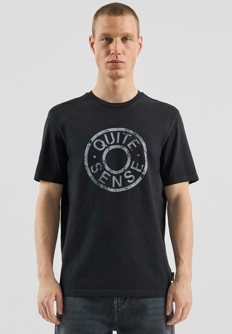 Czarna bawełniana koszulka z okrągłym nadrukiem w szarym kolorze z napisem „QUIET SENSE.” Okrągły dekolt, krótkie rękawy i luźny krój.