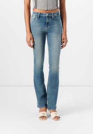 Jean en denim bleu clair au design ajusté, avec une légère décoloration et des jambes droites. Associés à des talons ouverts beiges avec un accent de logo.