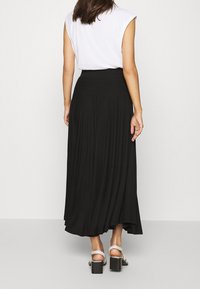 Musta maksihame pehmeästä kankaasta, jossa on korkea vyötärö ja valuva pleat. Yhdistetty valkoisen hihattoman topin ja paksupohjaisten sandaalien kanssa.