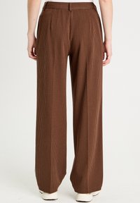 Pantaloni larghi beige con un leggero motivo a quadri, dotati di due pieghe frontali e una cintura liscia. Realizzati in tessuto testurizzato.